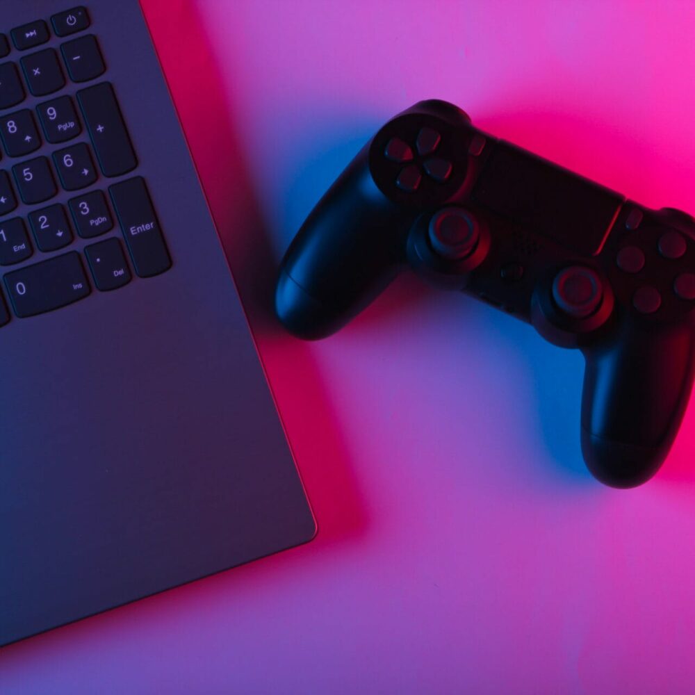 Laptop and gamepads with blue pink neon vibrant light. Gaming, leisure and entertainment concept. Top view